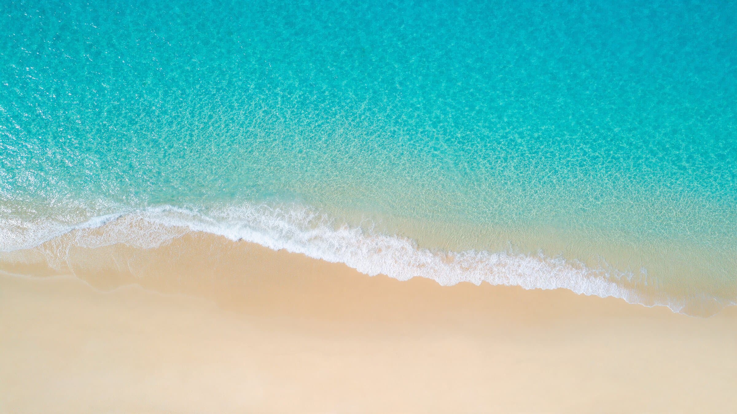 Turquoise water and white surf washing onto pale sand, seen from above