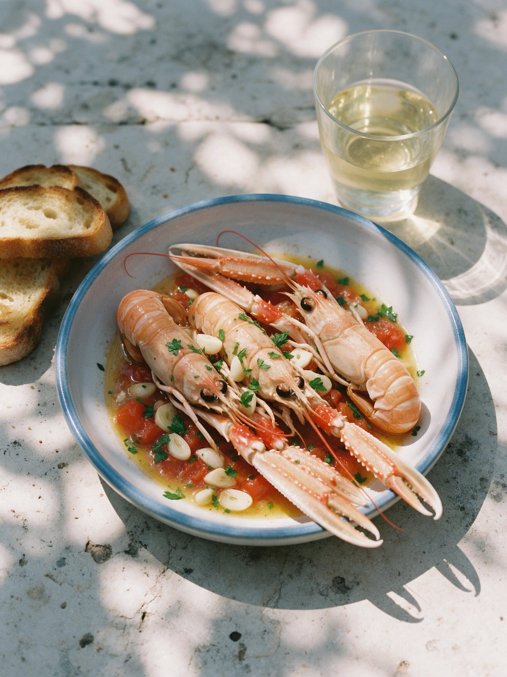 Kvarner scampi buzara in a blue-rimmed dish with toasted bread and white wine